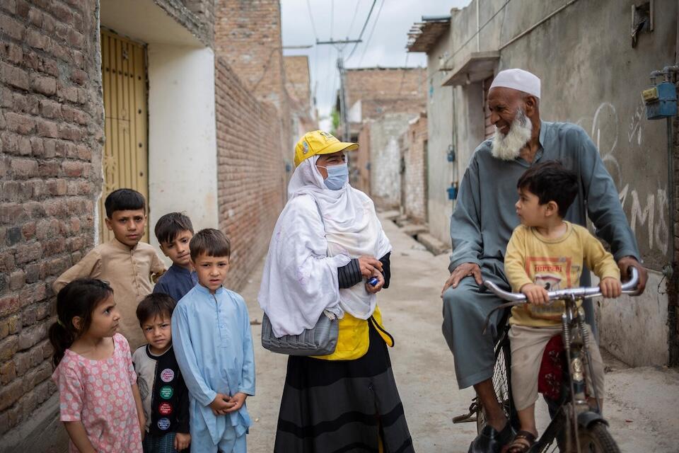 On April 18, 2023 in Peshawar, Khyber Pakhtunkhwa province, Pakistan, Lady Health Worker (LHW) Shamim Hussain, center, speaks with a man and a child on a bicycle while a group of children look on.